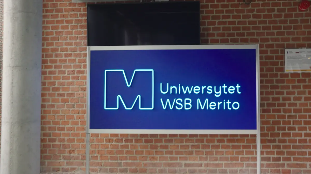 Neonowe logo Uniwersytetu WSB Merito na ceglanej ścianie kampusu w Poznaniu