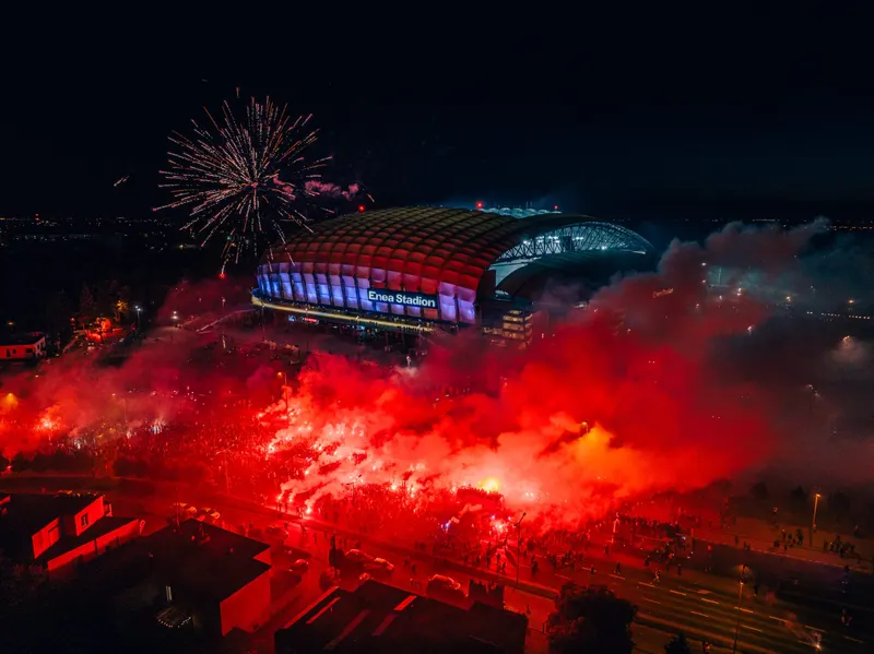 Enea Stadion nocą, rozświetlony stadion i czerwone race na pierwszym planie